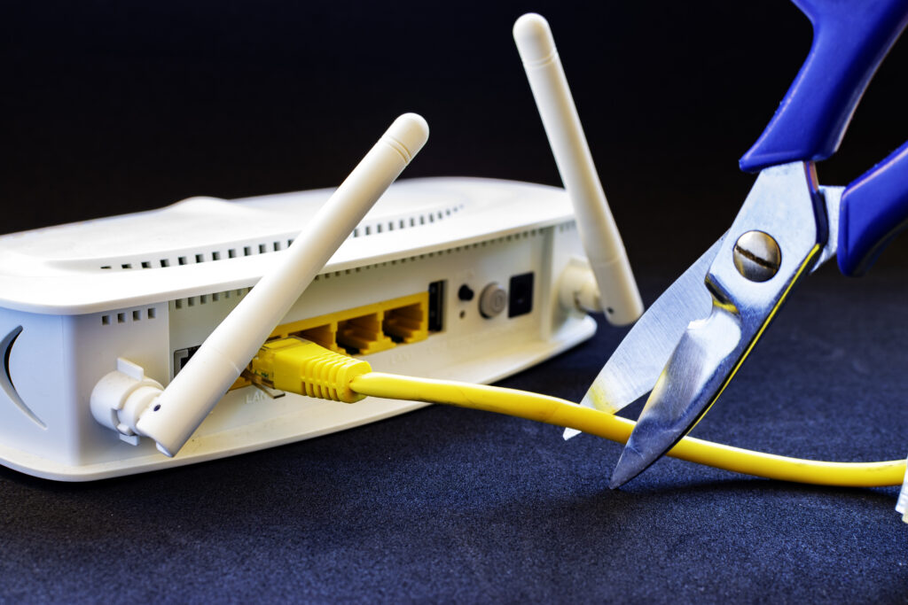 Action of cutting a yellow network cable with blue scissors.