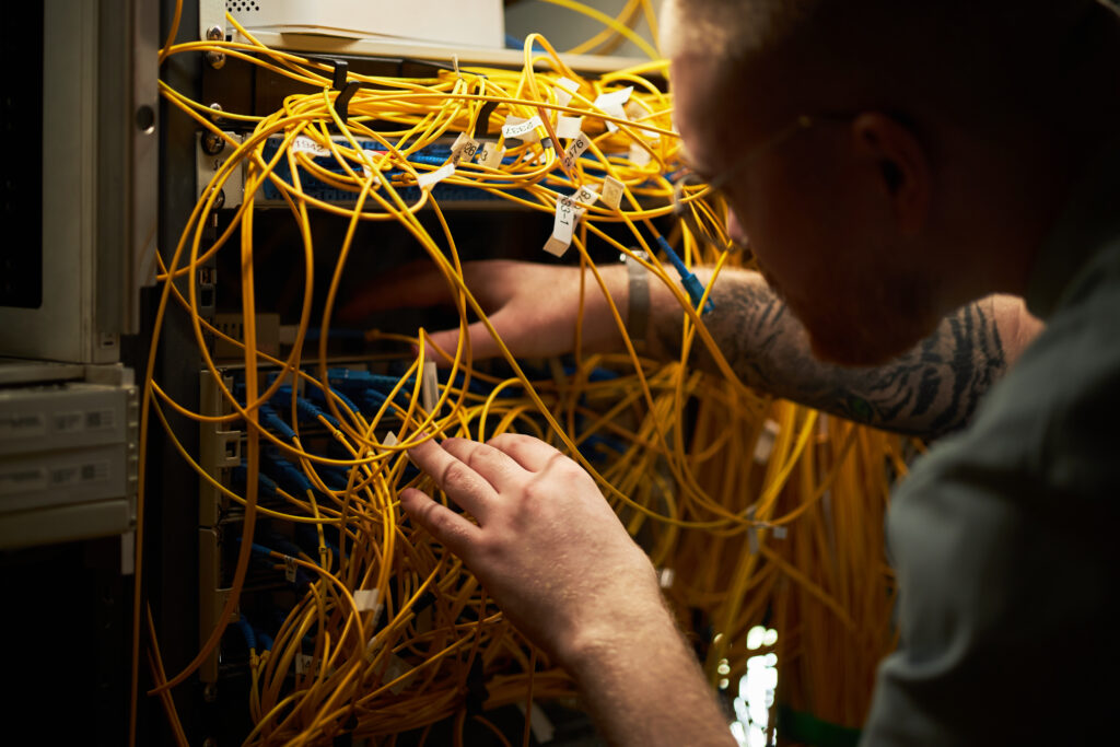 Man working with network cables and server equipment in server room during maintenance check, focused on ensuring proper connections among intricate wiring