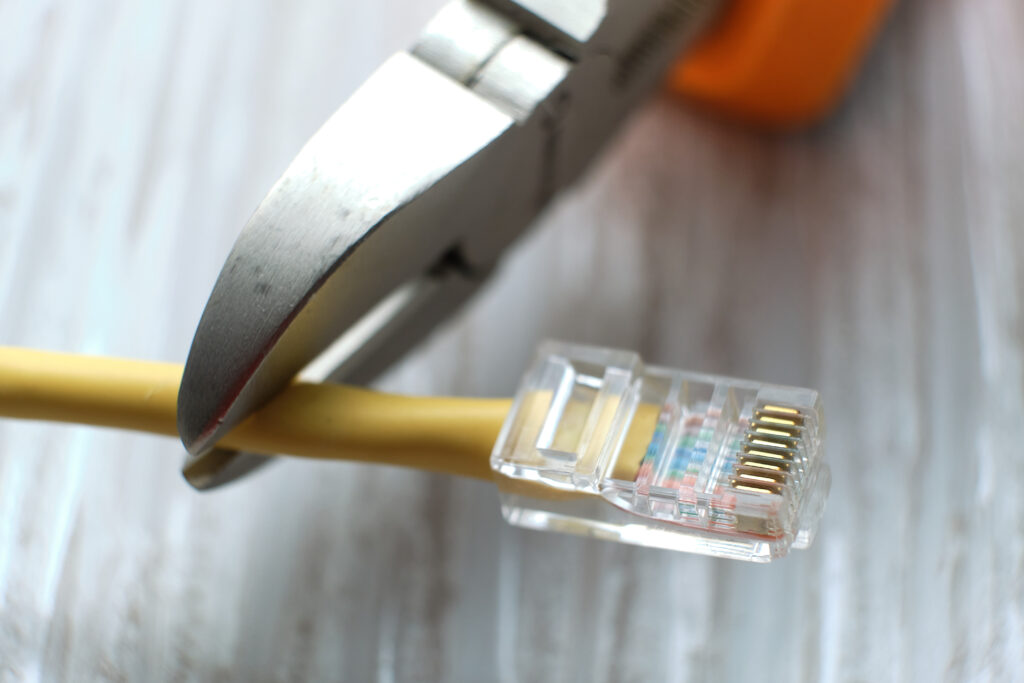 wire cutters cutting internet cable. Connection plugs and wires on old wooden background. Concept of global internet outage